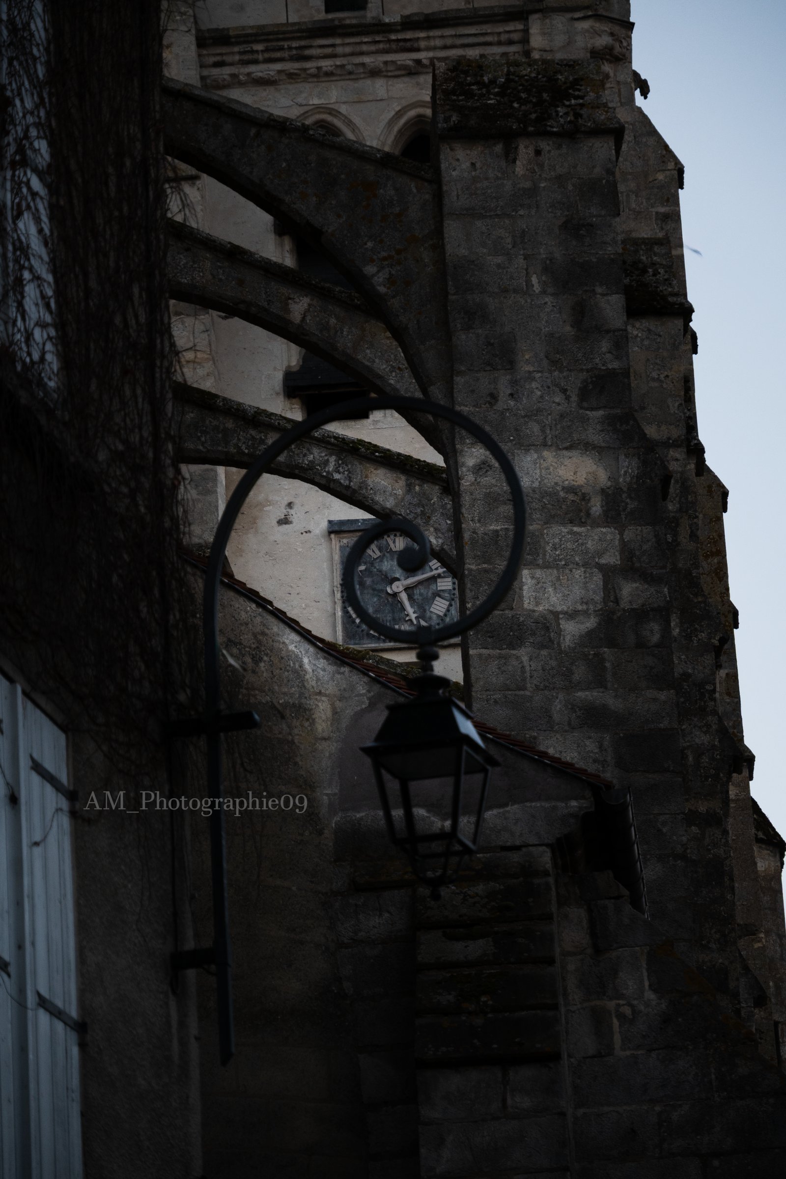 Horloge du clocher de l'église de Dourdan encadrée par un lampadaire ancien