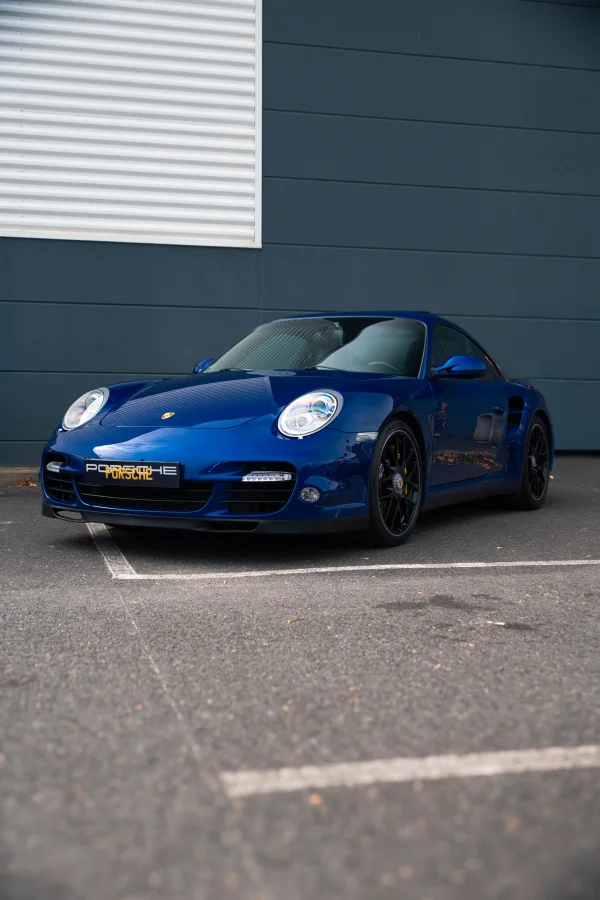 Porsche bleu profond devant un mur gris, vue de trois quarts